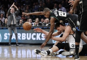 Brooklyn Nets center Brook Lopez on the floor and Milwaukee Bucks guard/forward Khris Middleton falling over Lopez struggling for the ball.